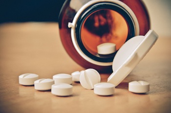 Bottle of pills on table top with pills spilling out.